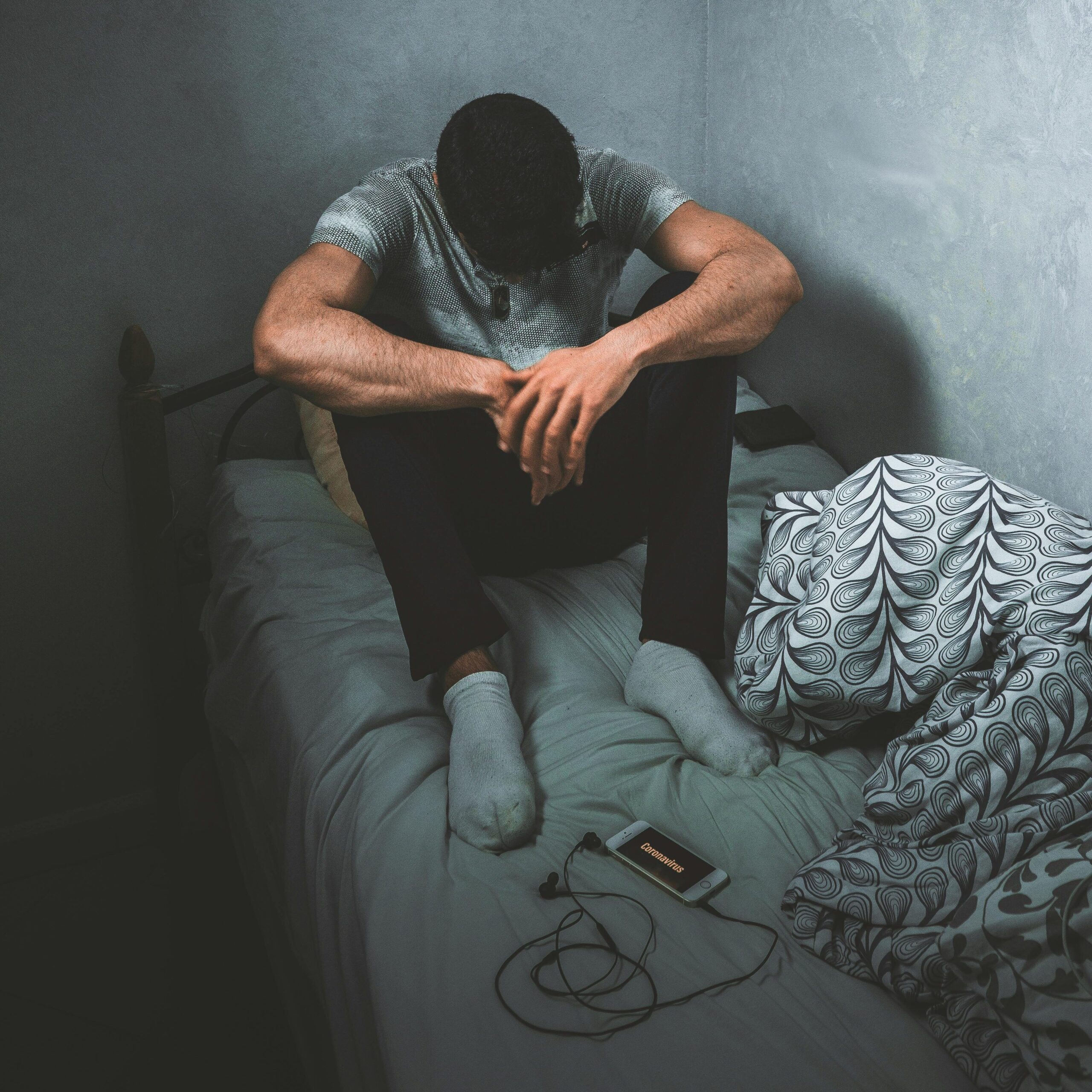 A man sits pensively on a bed in a dimly lit room, conveying emotion and introspection.